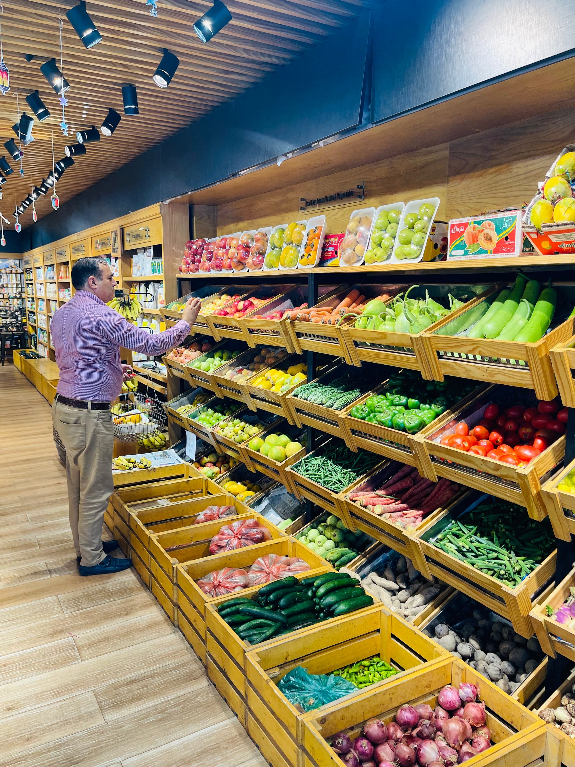 Man shopping in a grocery store with produce shelves filled with fruits and vegetables.